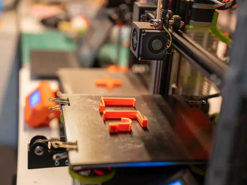 A 3D printer's print head over orange printed plastic parts on the build plate