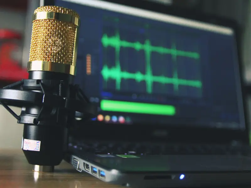 A gold studio microphone in front of a laptop showing green audio waveforms