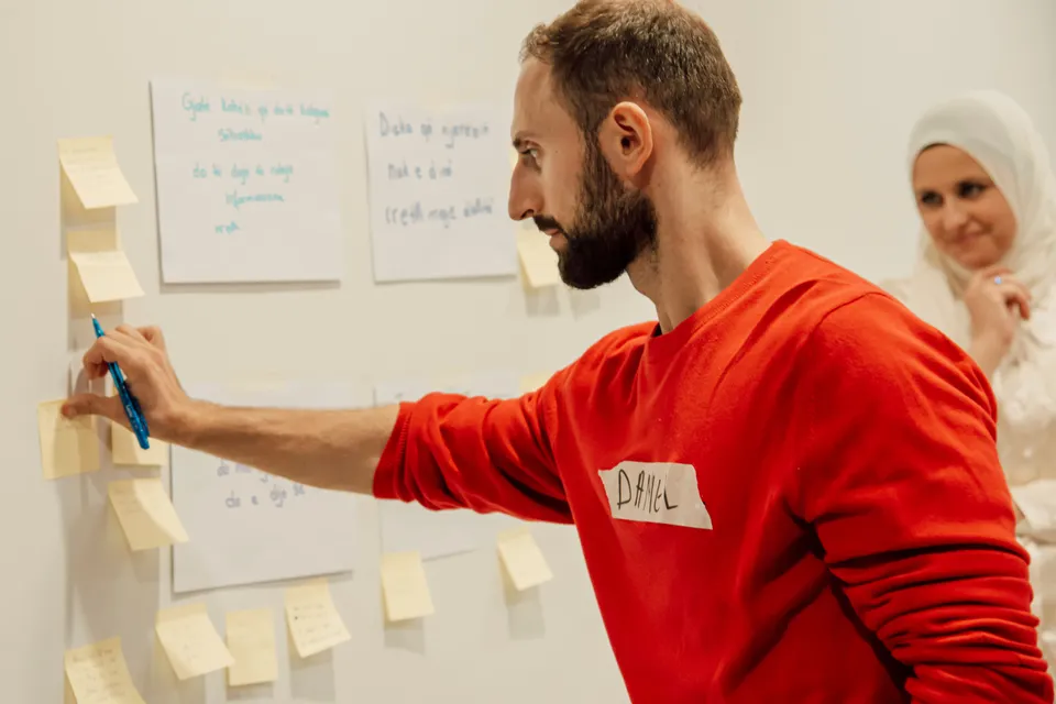A man sticking notes onto a planning wall while a colleague looks on.