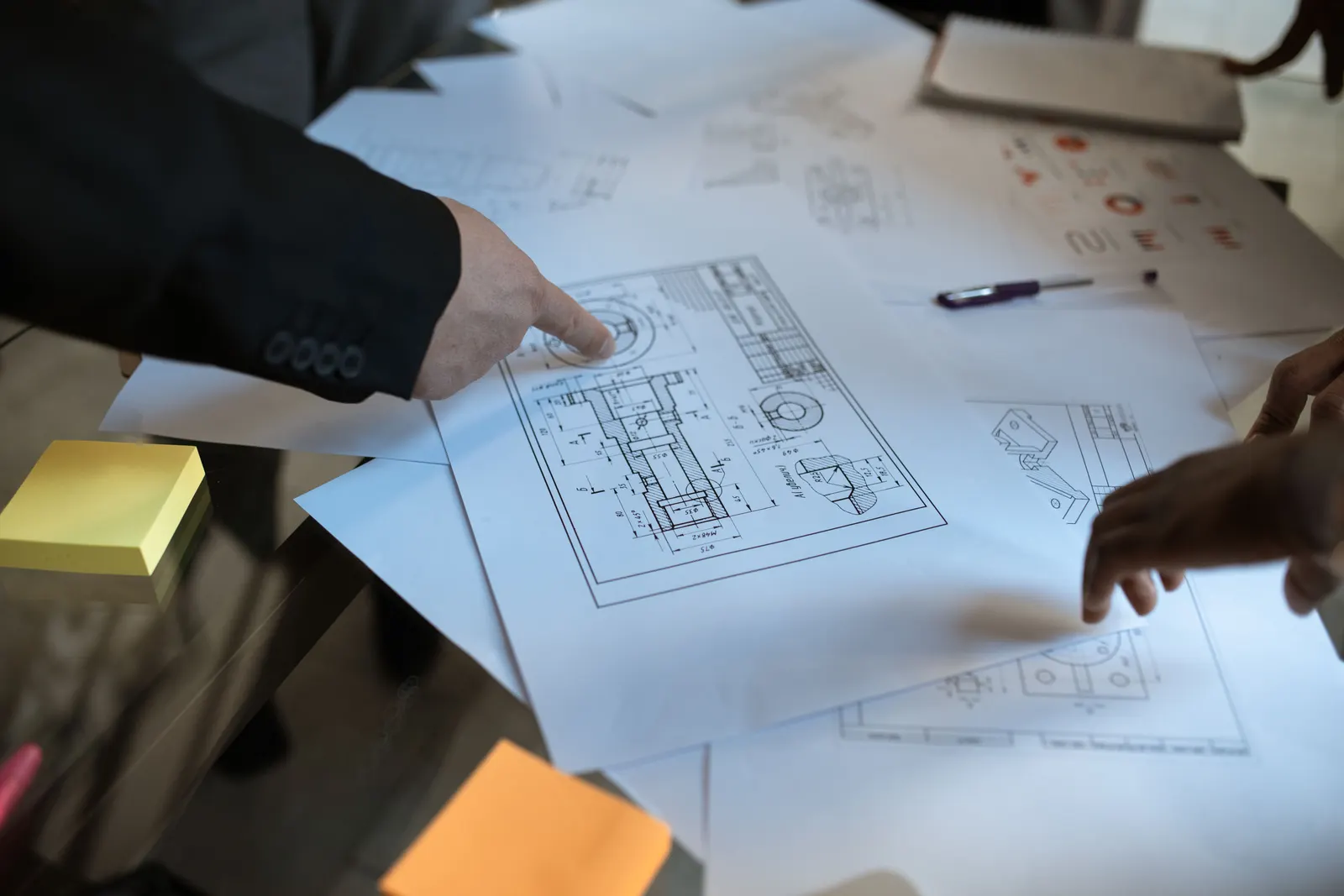Hands pointing at a floor plan spread across a desk during a design discussion.