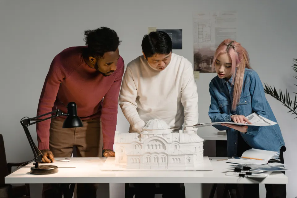 Three architects leaning over a white scale model of a building on a desk.