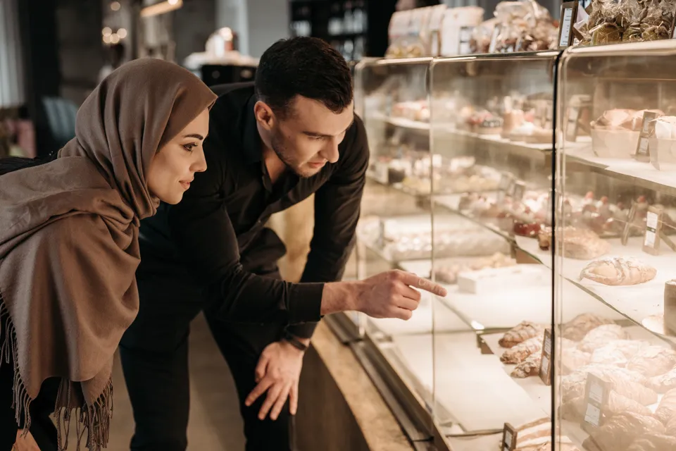 A couple leaning over a bakery's glass counter, choosing from the pastries on display.