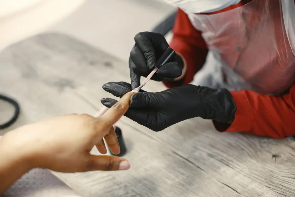 A nail technician in black gloves painting a customer's fingernails.