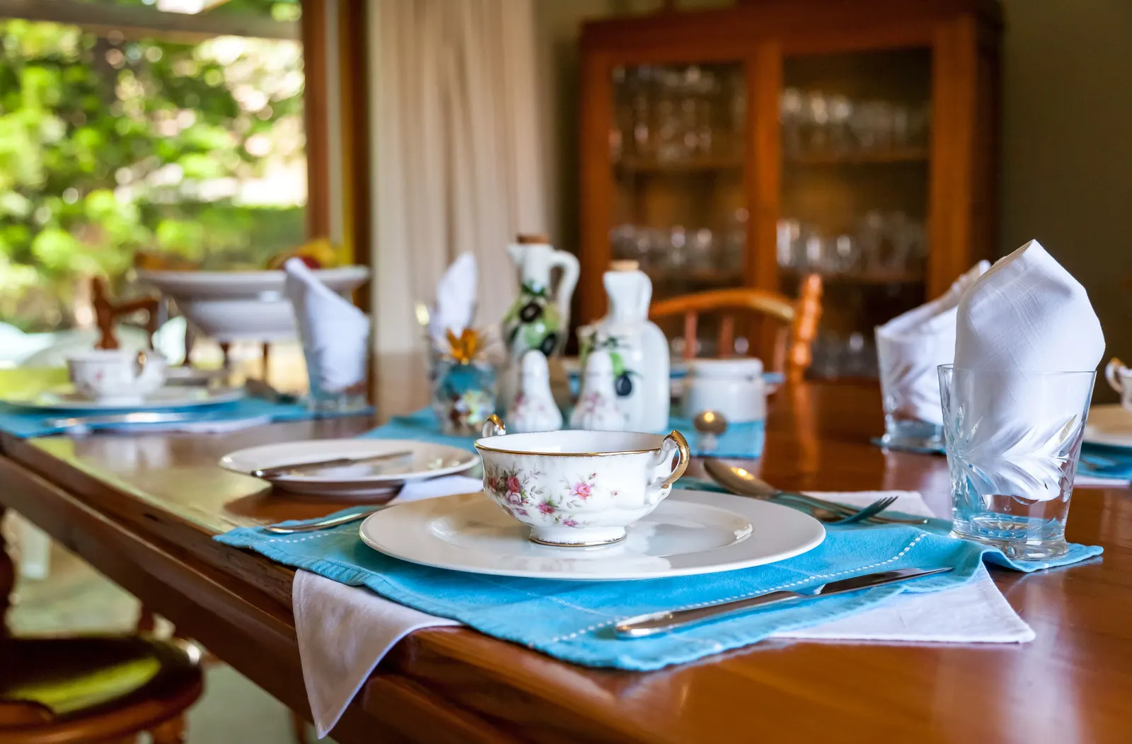 A breakfast table laid with china cups, folded napkins and a teapot in a guest house dining room.