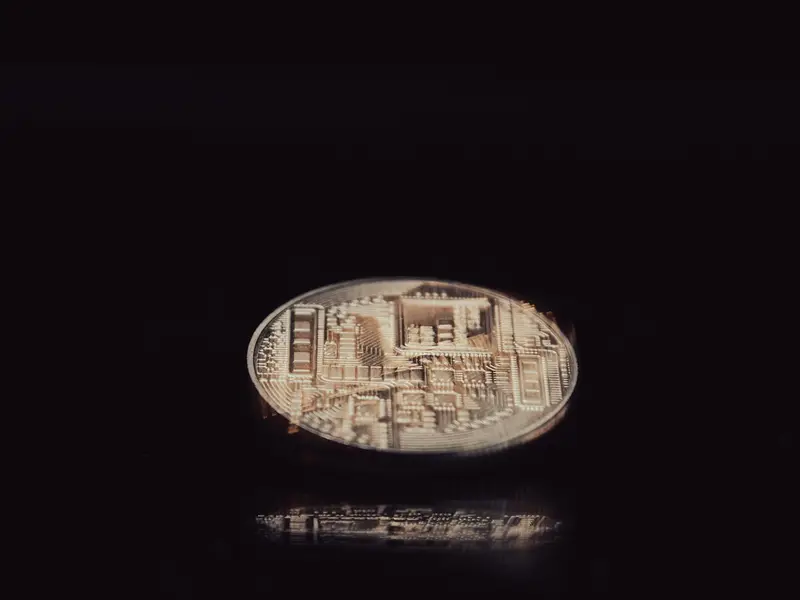 A single metal coin engraved with a circuit-board pattern, lit against a black background
