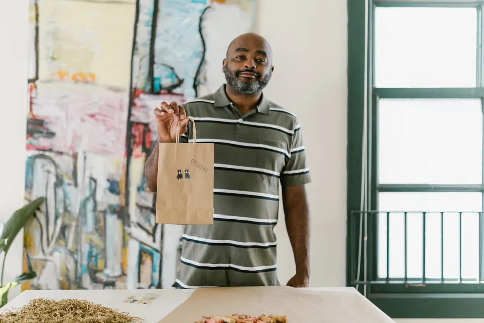 A smiling business owner holding up a paper bag with his own sticker on it.