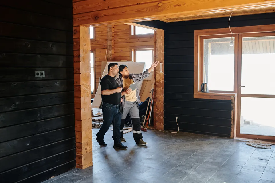 Two people walking through a timber-framed room that is still being fitted out.