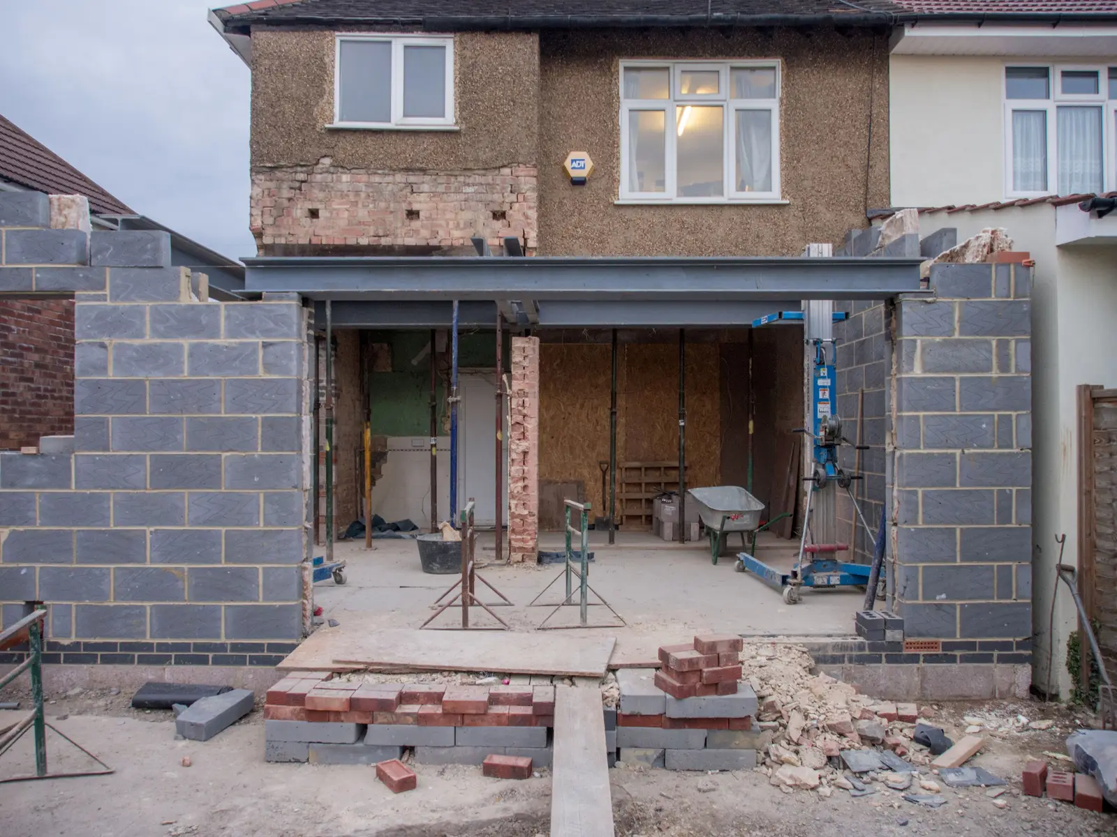 A rear extension under construction on a brick house, with blockwork walls and materials in the garden.