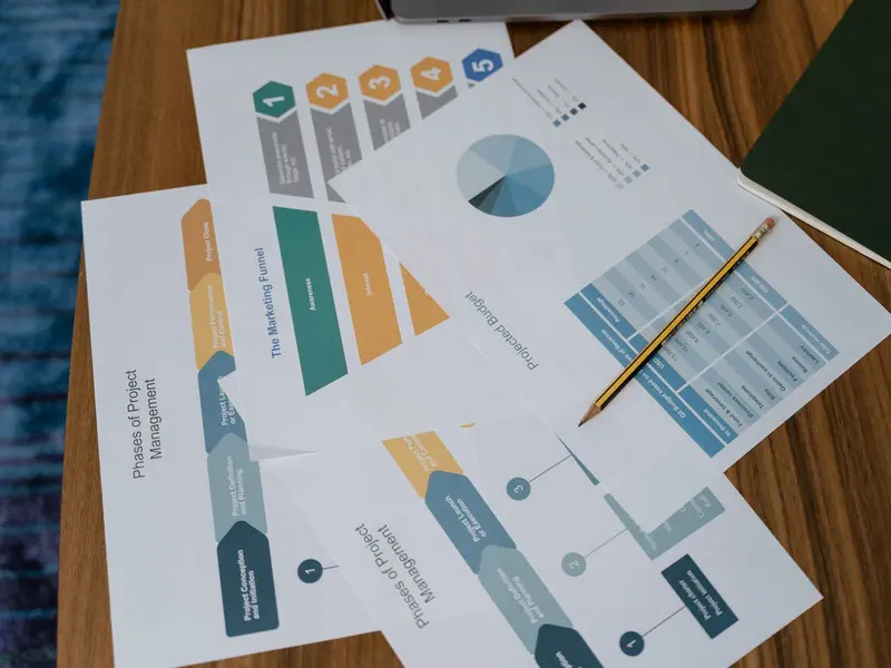 Printed pages of charts and process diagrams spread on a wooden meeting table with a pencil