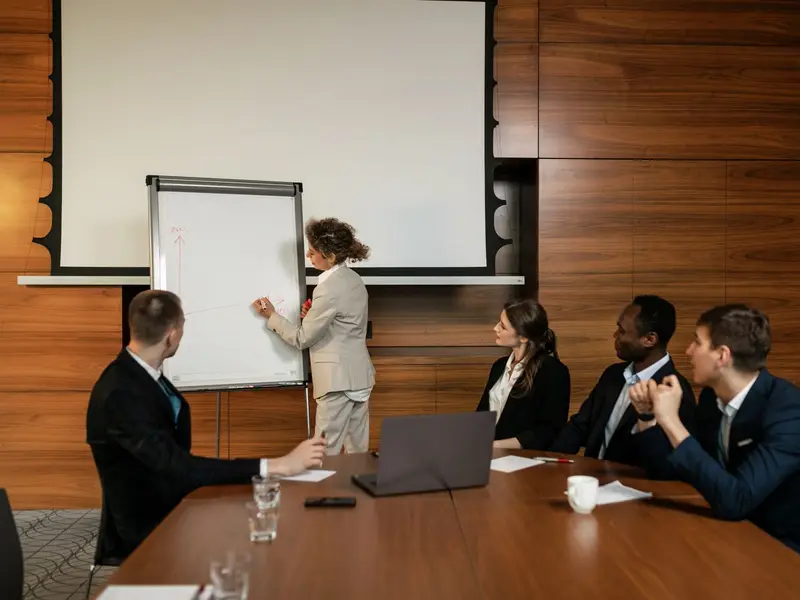 A woman presenting at a flip chart to four colleagues around a boardroom table