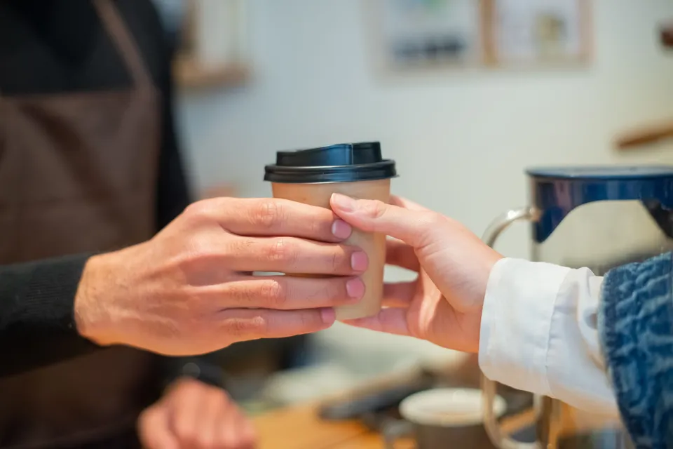 A barista handing a takeaway coffee across the counter to a customer.