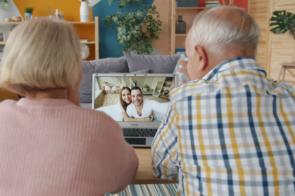An elderly couple on a video call with younger relatives on a laptop.