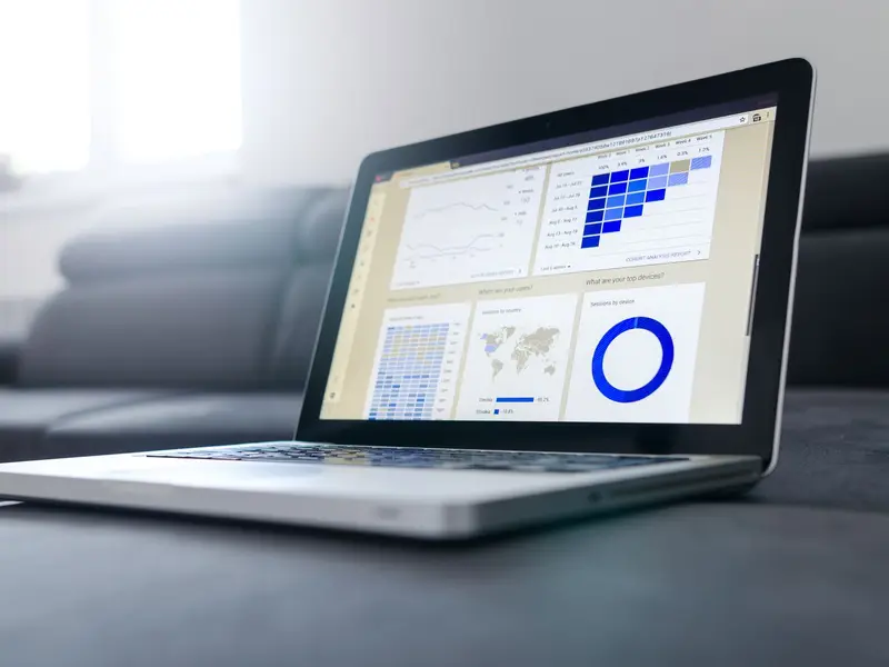 A laptop on a sofa showing a dashboard of charts, a map and a ring chart