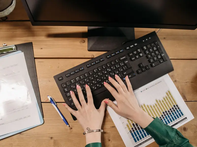 Overhead view of hands typing on a keyboard beside a clipboard and a printed bar chart
