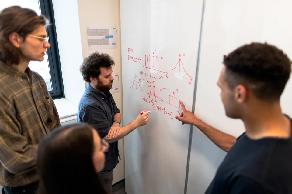 A team gathered at a whiteboard while one person draws a diagram of connected steps.