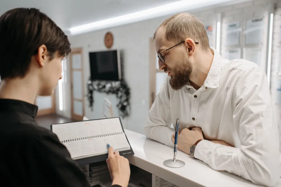 A patient at the reception desk while the receptionist writes in the appointment book.