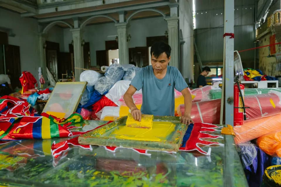 A man screen-printing onto fabric in a busy textile workshop.