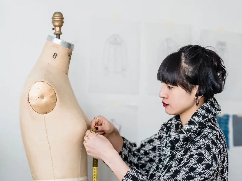 A fashion designer pinning fabric to a tailor's dress form in a studio