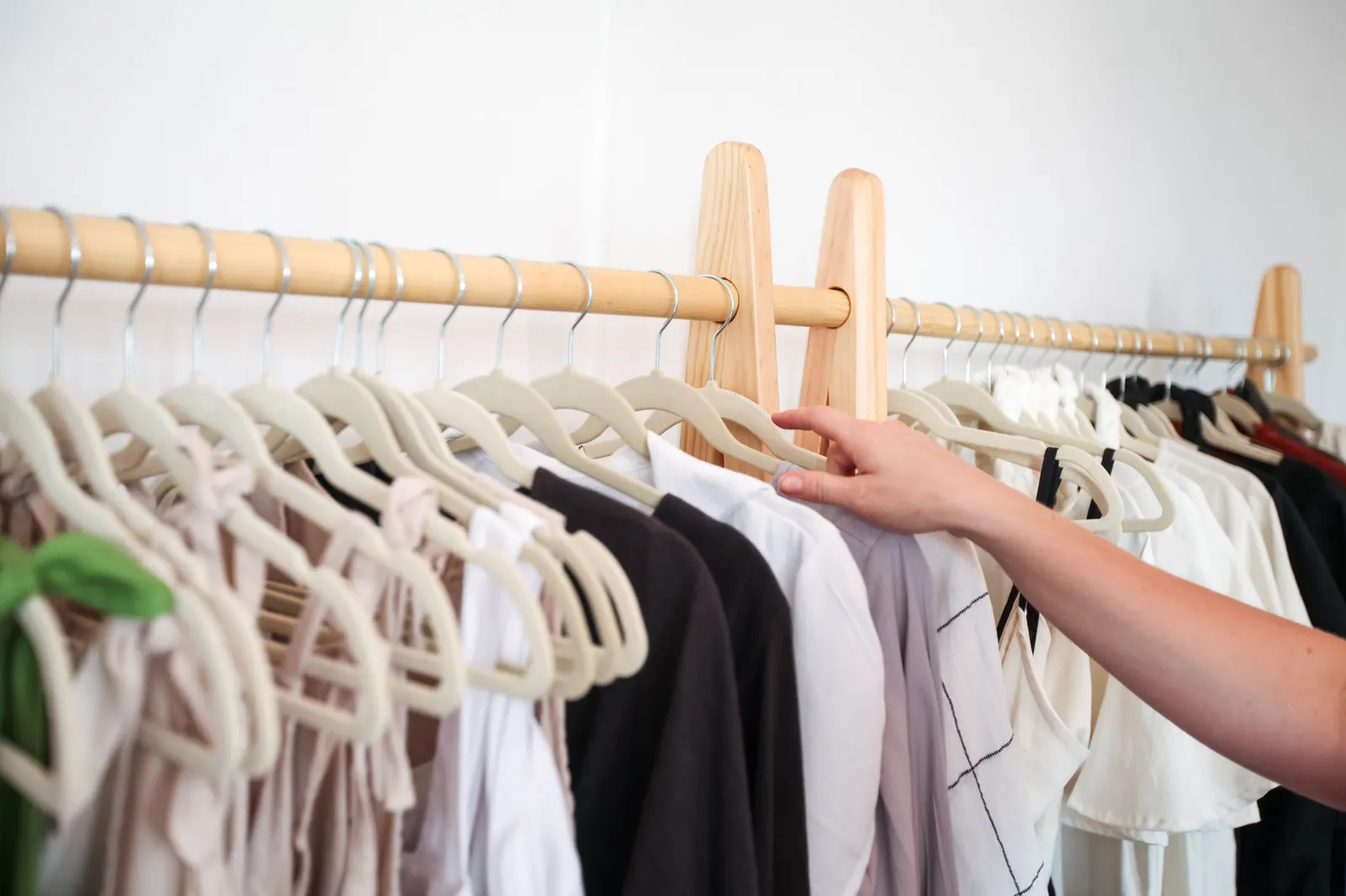 A hand browsing a neat rail of clothes on hangers in a small boutique.