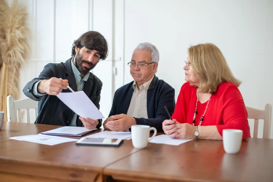 An adviser pointing out a line on a printed document to an older couple at a table.