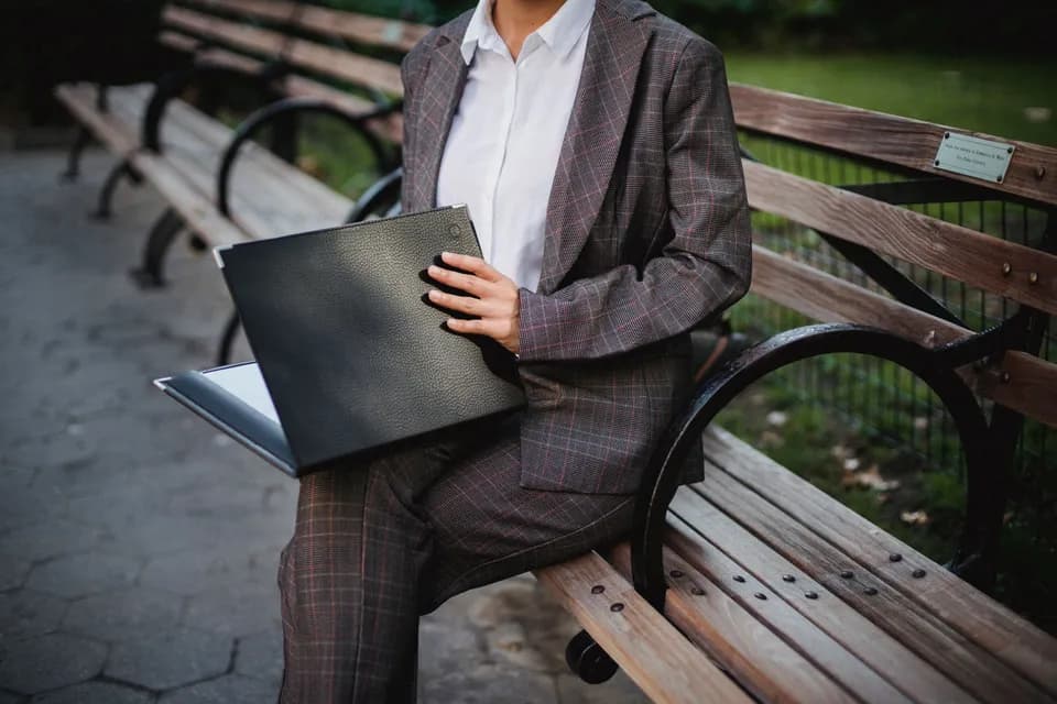 A woman in a checked suit sitting on a bench with a folder, waiting before an appointment.
