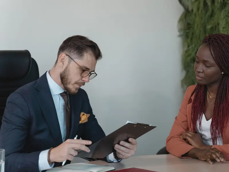 A job interview: a man reading a candidate's papers on a clipboard across a desk from her