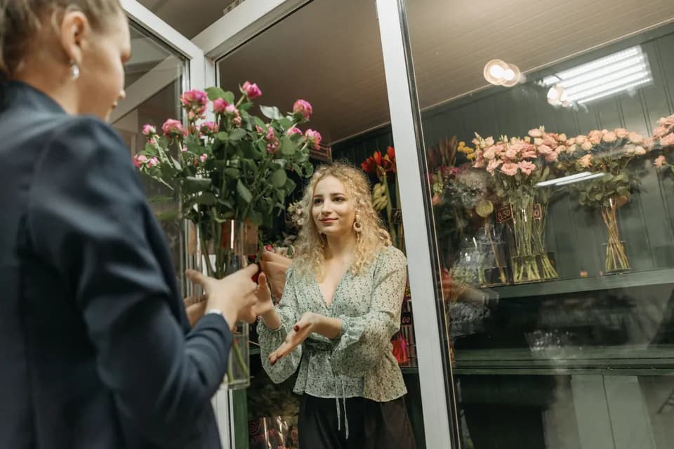 A florist handing a customer a bunch of roses at the door of a flower shop.