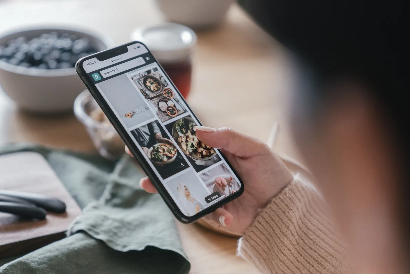 A hand scrolling a page of food dishes on a phone at a kitchen table.