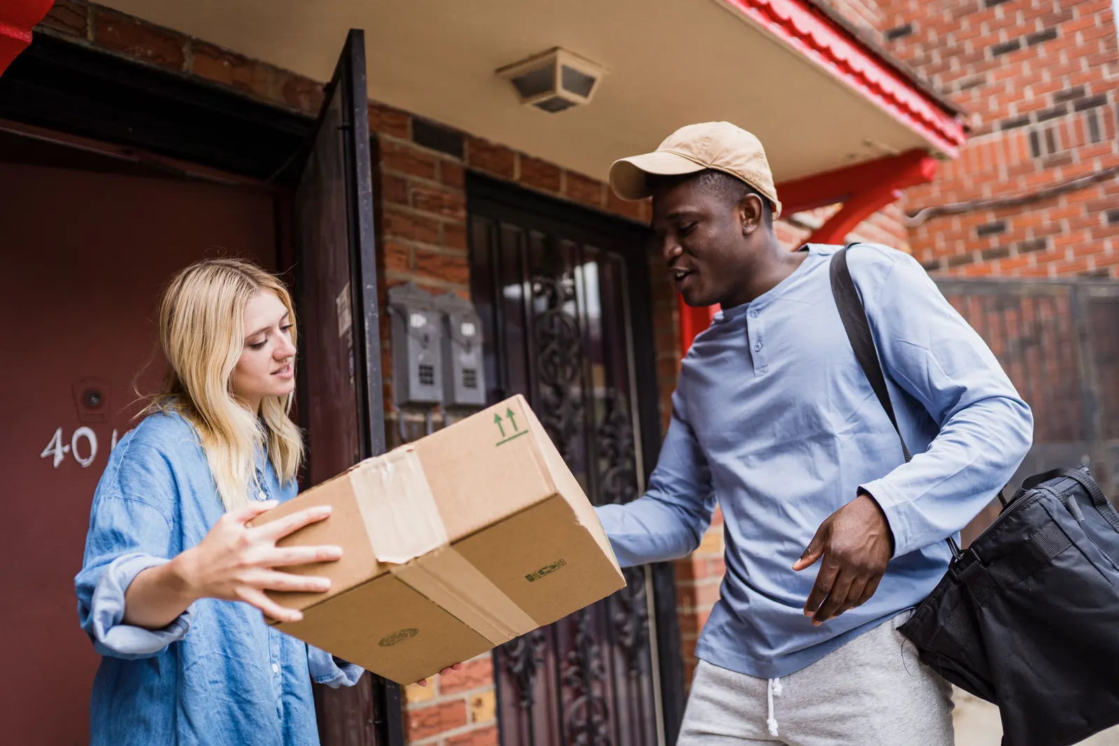 A courier handing a cardboard parcel to a woman at her front door.