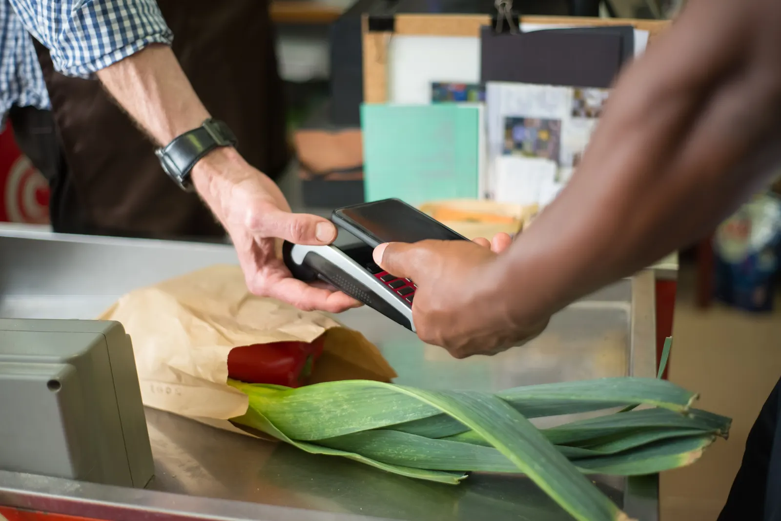 A customer tapping a phone on the card reader to pay at a grocery counter.