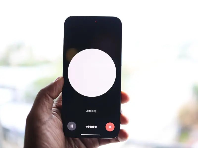 A hand holding a phone with an AI assistant listening, a glowing circle on screen