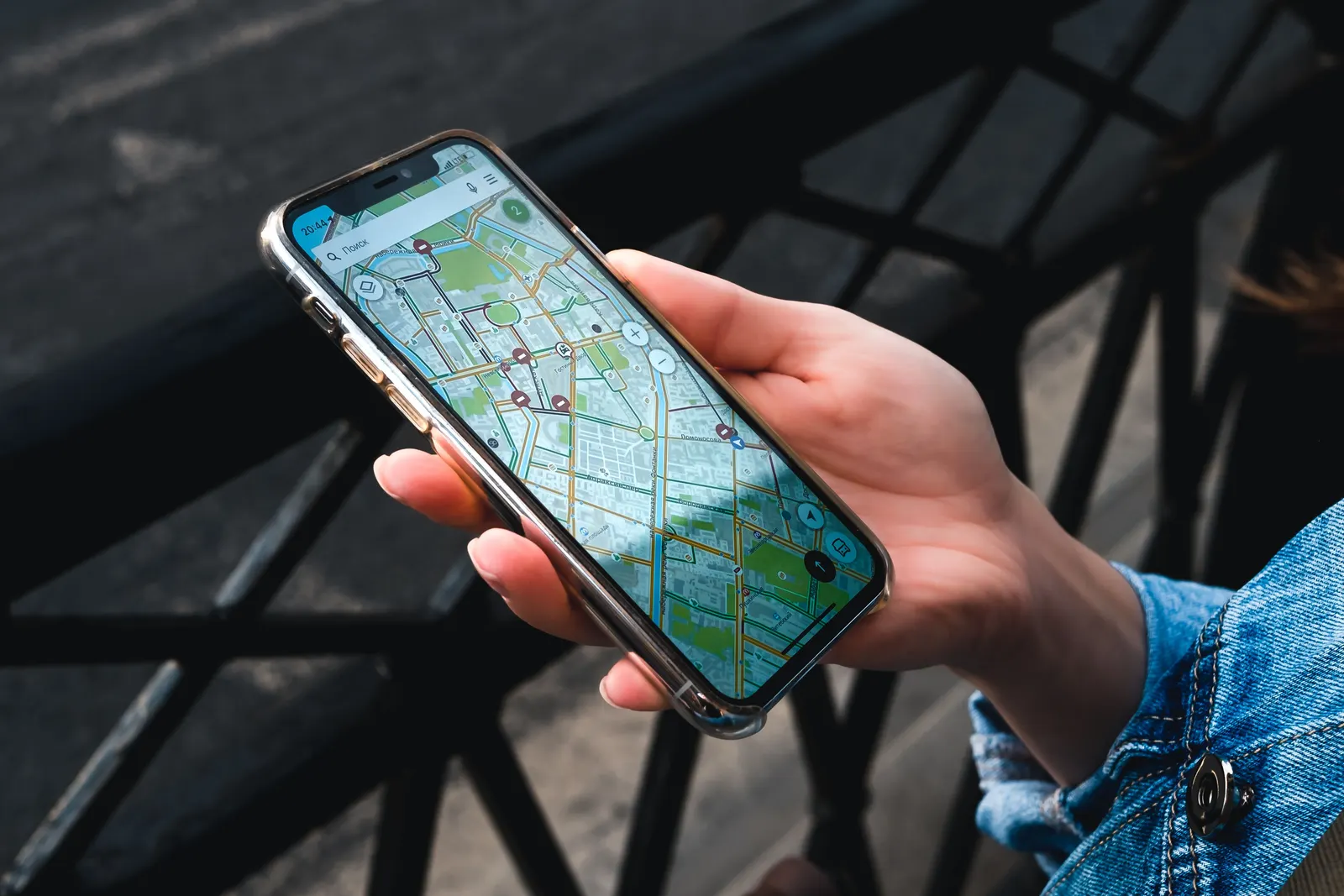 A hand holding a phone with a street map open, over a railing outdoors.