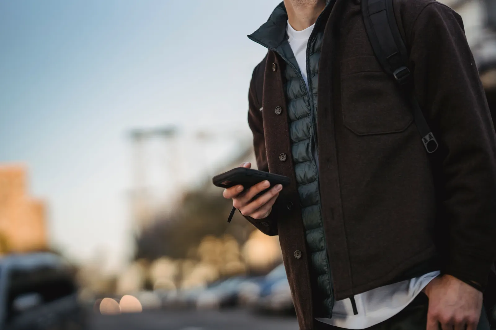 A man in a jacket checking his phone while standing in the street.