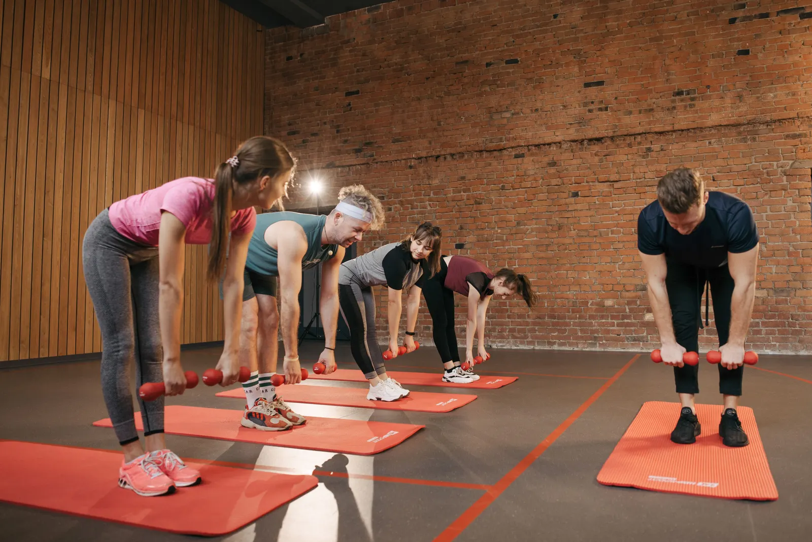 A group exercise class working with dumbbells on mats in a studio with brick walls.