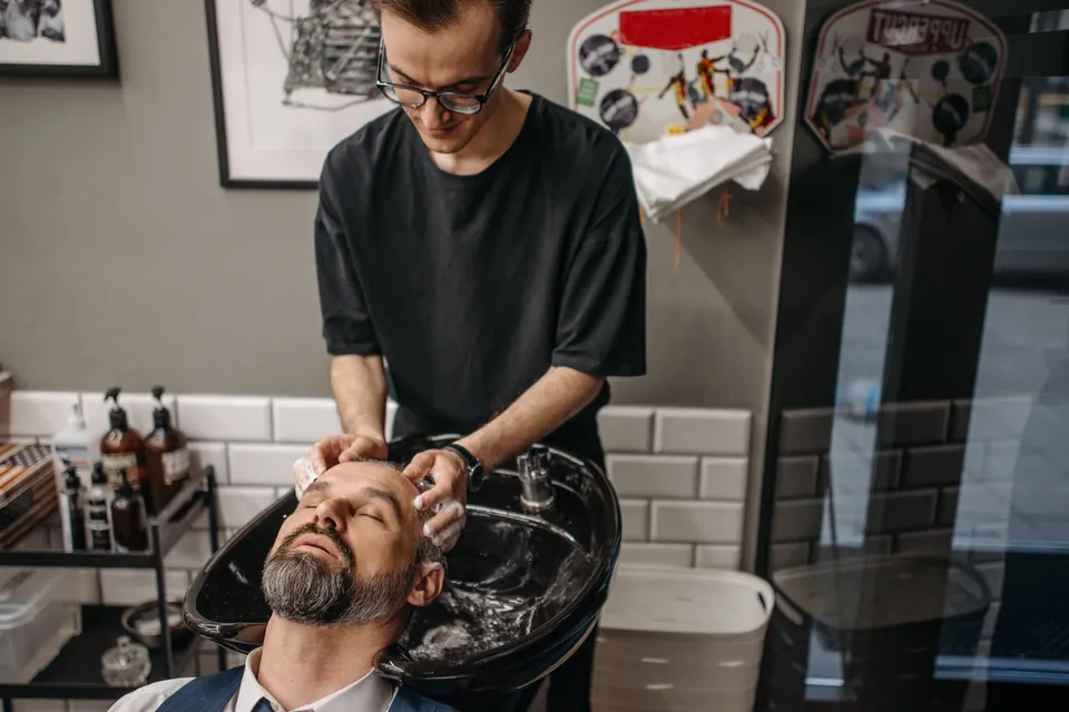 A barber washing a customer's hair at the basin before a cut.