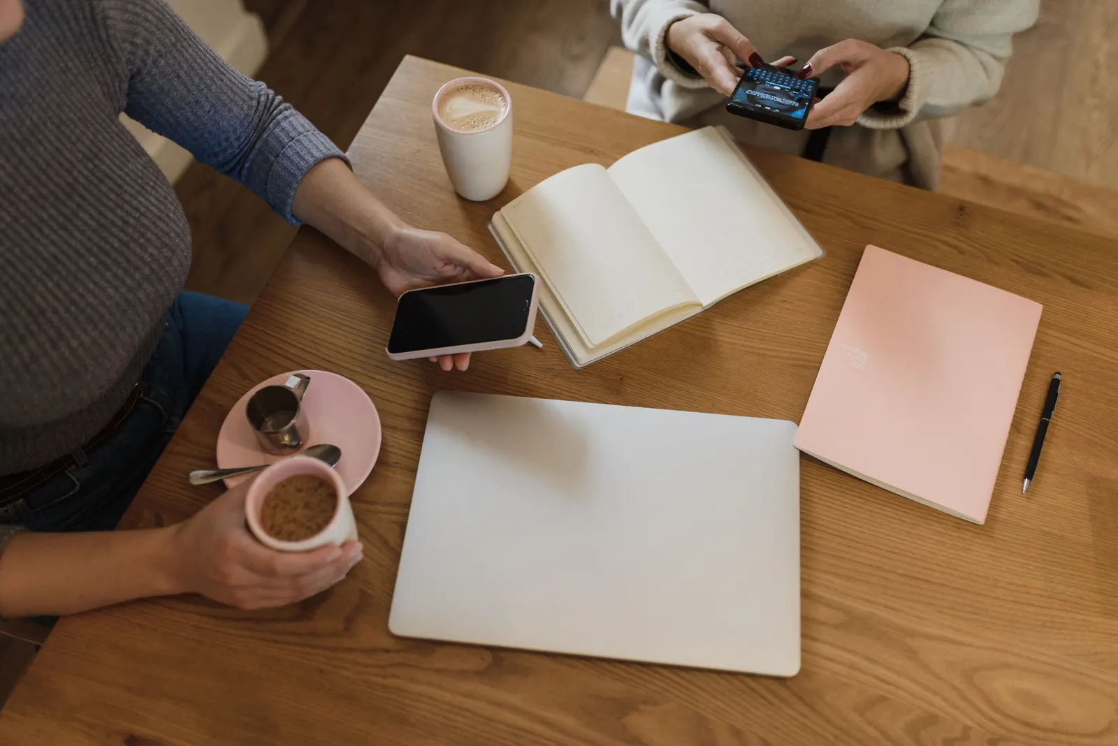 Two people at a cafe table with coffee, open notebooks and phones between them.