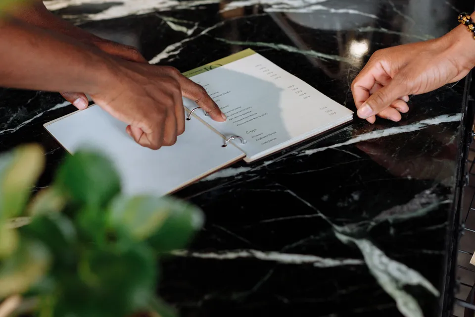 Two people's hands going over a printed menu on a marble counter.