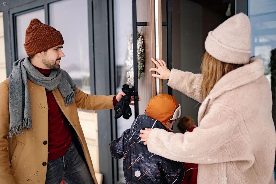 A family in winter coats letting themselves in at the front door of a house.
