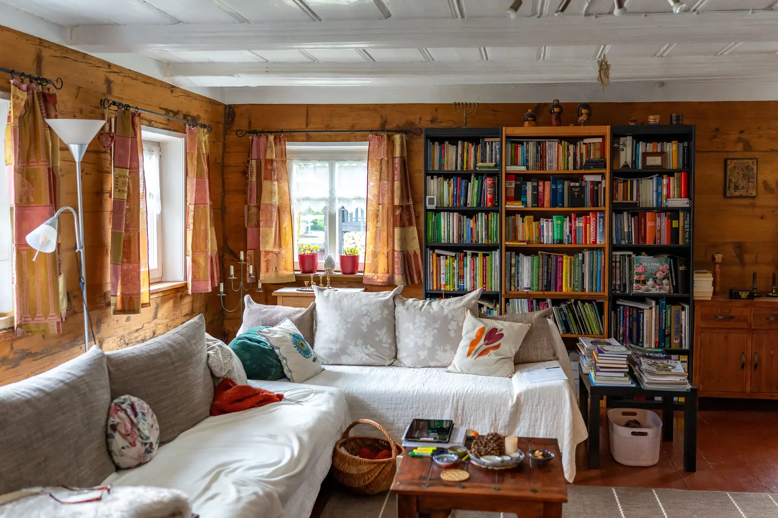 A cottage living room with a sofa, cushions and a wall of bookshelves, ready for guests.