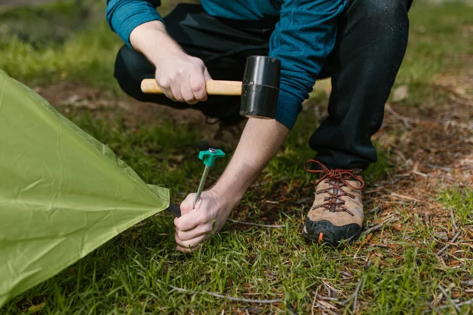 A camper hammering a peg into the grass to hold down a tent.