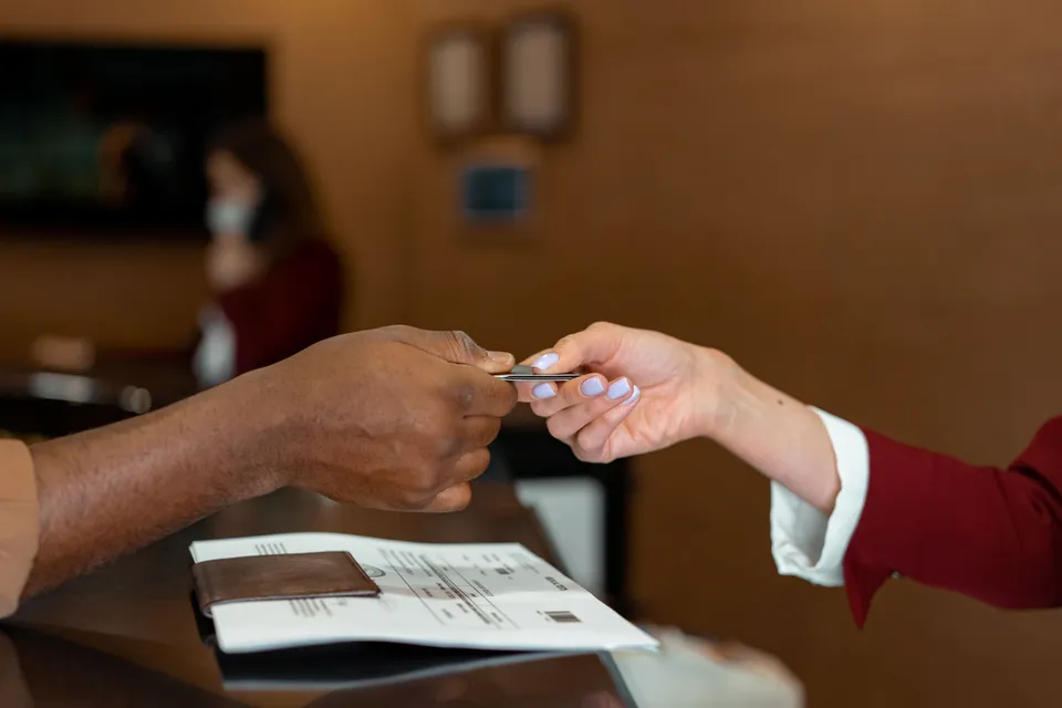 A guest handing a card to the receptionist across a hotel front desk at check-in.