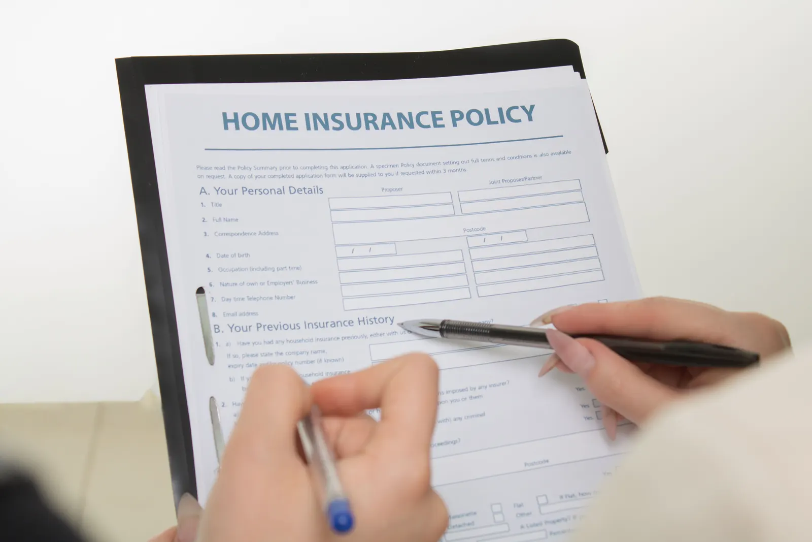 Hands filling in a home insurance policy form with a pen.