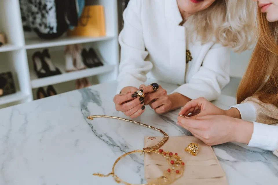 Two women looking over gold necklaces and rings laid out on a marble counter.