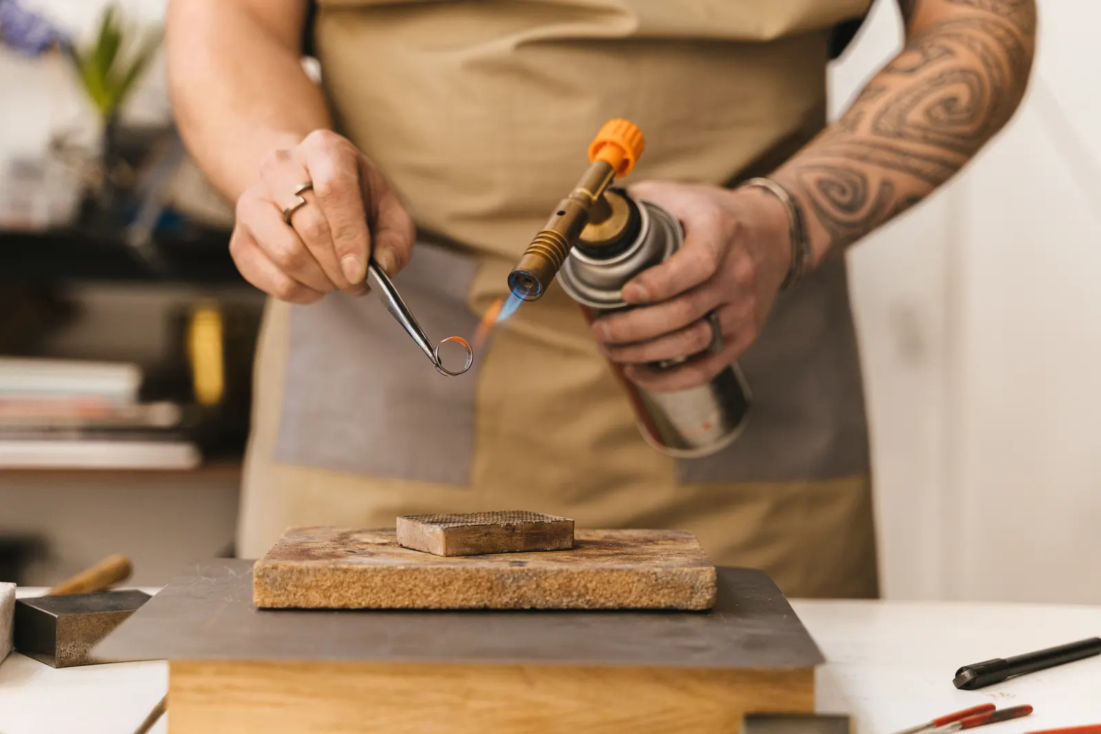 A jeweller at the bench using a small torch to work on a ring.