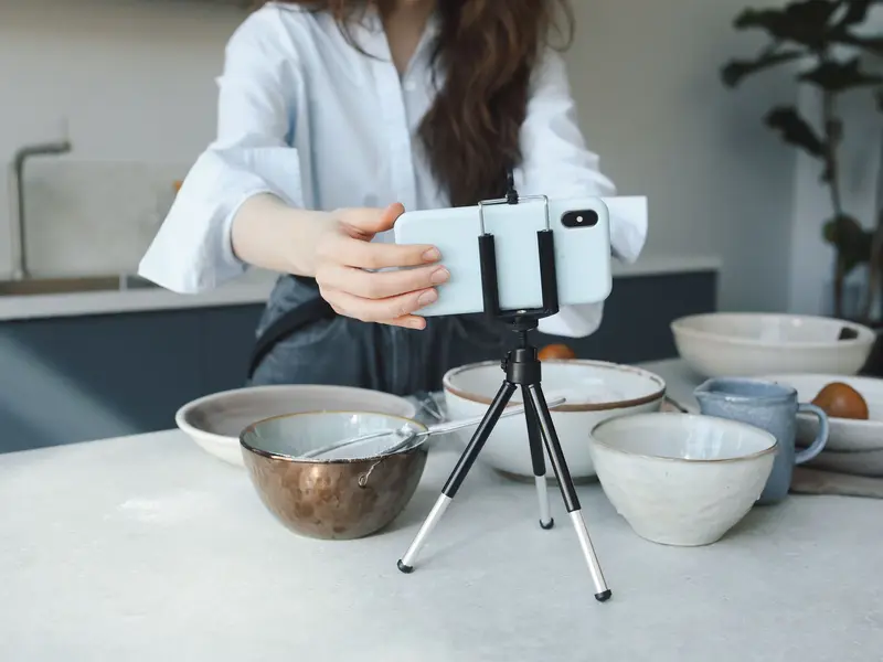 A woman setting a phone on a small tripod to film bowls on her kitchen counter