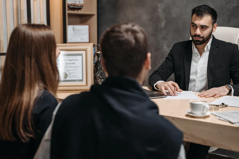 A lawyer at his desk going through documents with two clients sitting opposite.
