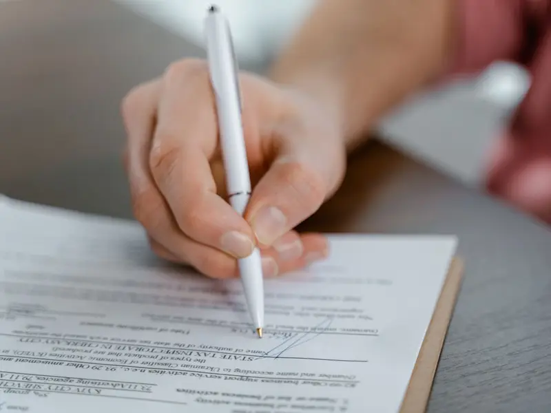 A hand signing a printed document with a white pen
