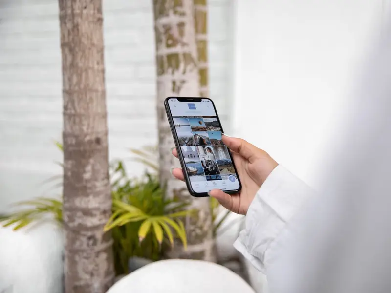 A hand holding a phone that shows a grid of social media posts