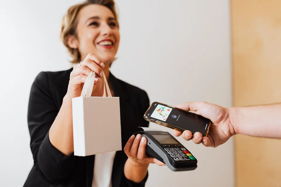 A shop assistant handing over a bag as a customer pays by tapping a phone on the card reader.