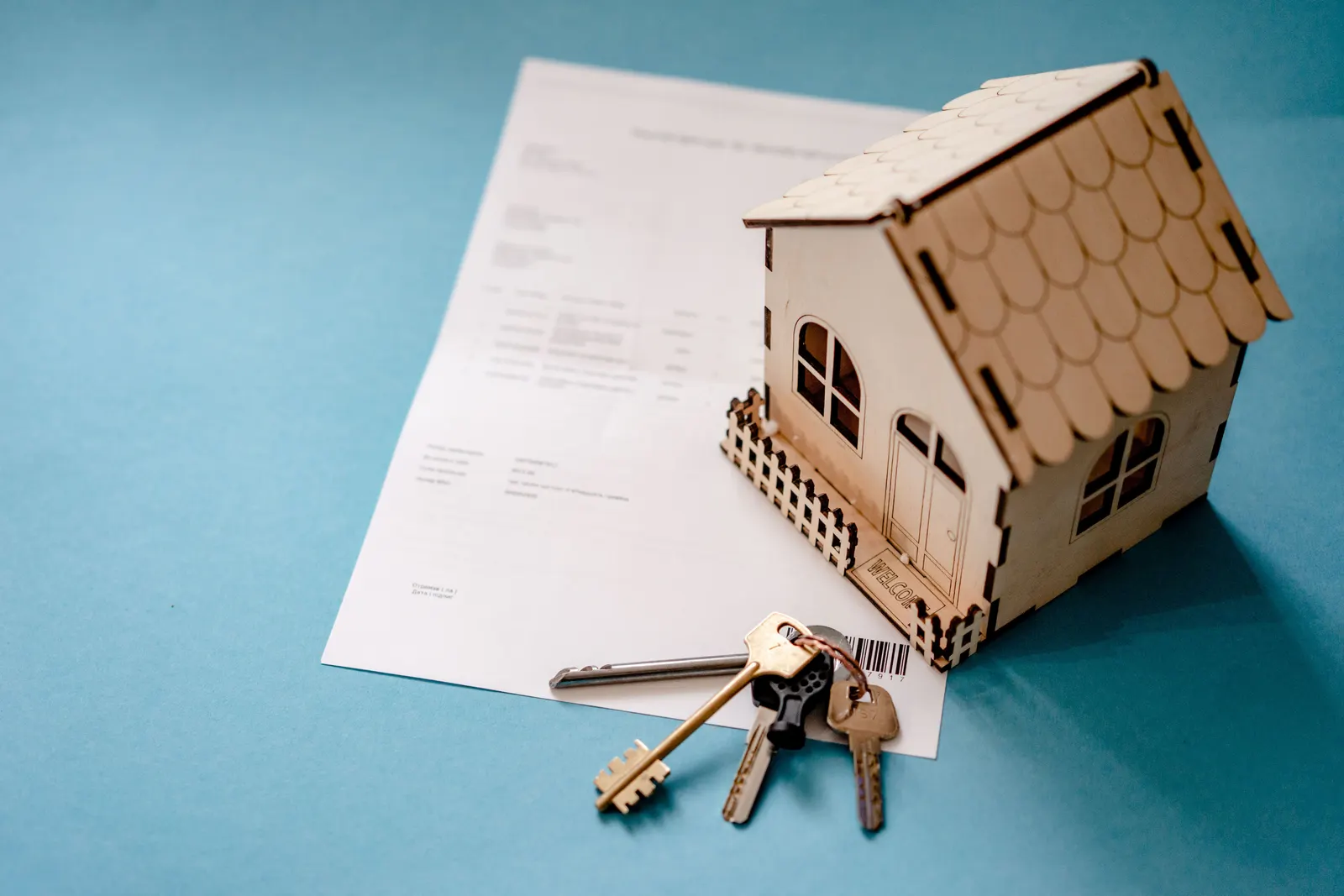 A small wooden model house beside a set of keys and a signed contract.
